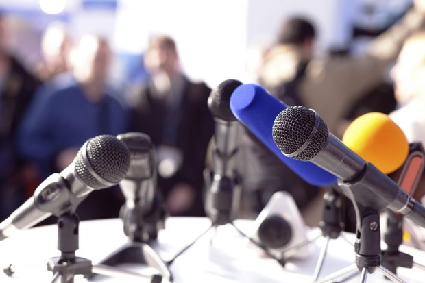 microphones and a blurred background of what looks like a press conference