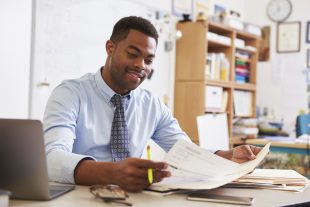 a teacher holding a paper he is marking, and looking quite happy with himself about it