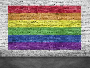 Rainbow flag painted over old white brick wall