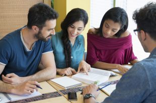 Closeup shot of young man and woman discussing on note. Happy and smiling student studying at the library. Multi ethnic group studying on book for the next exam.