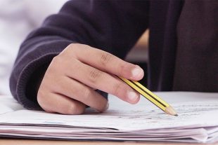 a child's hand holding a yellow pencil